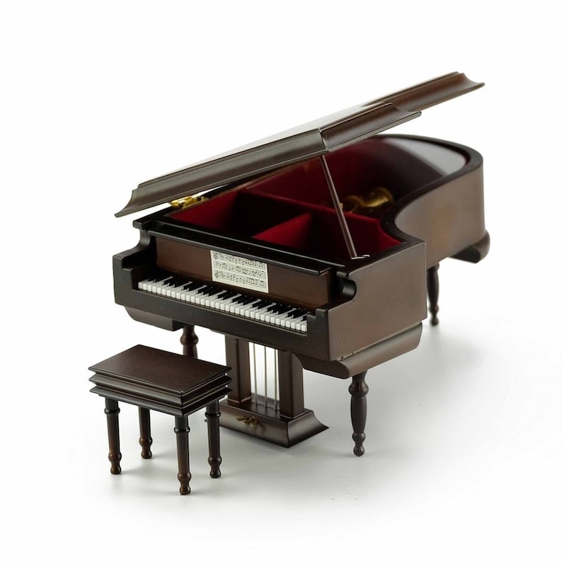 May include: A dark brown wooden grand piano music box with a red velvet interior and a matching stool. The piano has a hinged lid that is open, revealing the music box mechanism.