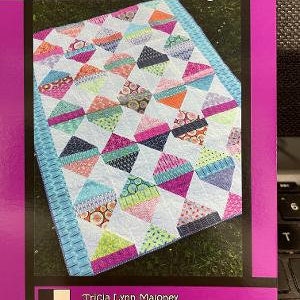 May include: A quilt pattern called "Diamond Daze" by Tricia Lynn Maloney for Villa Rosa Designs. The quilt pattern features a colorful diamond pattern with a variety of colors and fabrics.