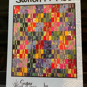 May include: A quilt pattern titled "Switch-A-Roo" with a colorful patchwork design. The quilt features squares in various colors including red, yellow, purple, and green. The pattern is from Sugar Pine Quilt Designs for Villa Rosa Designs.