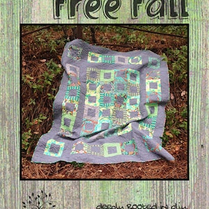 May include: A quilt with a "free fall" design in shades of green, blue, and gray. The quilt is made with a variety of fabrics and patterns. The quilt is lying on a bed of pine needles. The text "Homegrown" and "deeply rooted in diy" are also visible in the image.