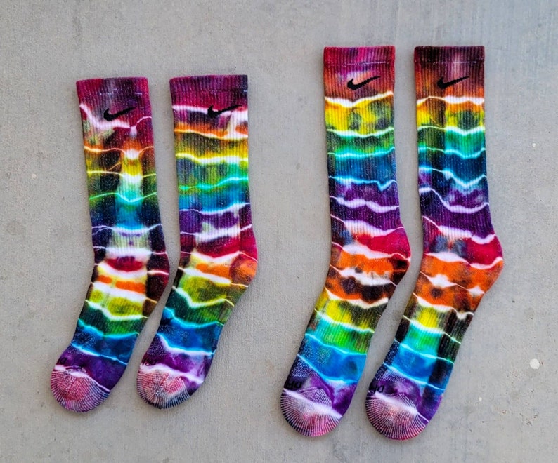 May include: Four colorful tie-dye socks with a black Nike logo on each. The socks are a mix of purple, blue, green, orange, and red.