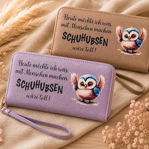 Könnte beinhalten: Zwei Reißverschluss-Geldbörsen, eine beige und eine lavendelfarbene, jeweils mit einem Cartoon-Eulen-Design. Die Geldbörsen haben eine Handschlaufe und deutschen Text. Die beige Geldbörse hat einen goldenen Reißverschluss.
