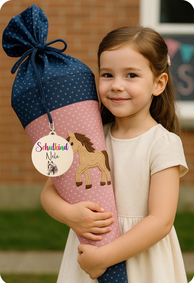 Pode incluir: Uma grande mochila escolar em forma de cone em rosa e azul marinho, decorada com um aplique de cavalo e uma etiqueta de madeira que diz "Schulkind Nele". A mochila &eacute; segurada por uma menina.