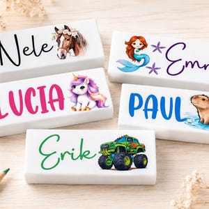 May include: White rectangular name blocks with colorful illustrations and names. The blocks feature a horse, unicorn, mermaid, capybara, and monster truck. Names include Nele, Lucia, Emma, Paul, and Erik.