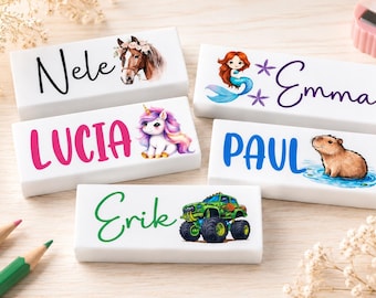 Op de afbeelding: Witte rechthoekige naamblokken met kleurrijke illustraties en namen. De blokken tonen een paard, een eenhoorn, een zeemeermin, een capibara en een monstertruck. Namen zijn Nele, Lucia, Emma, Paul en Erik.