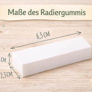 May include: A white rectangular eraser with dimensions of 2.56 inches long, 0.91 inches wide, and 0.51 inches high. The text "Ma&szlig;e des Radiergummis" is displayed above the eraser. The eraser is on a light wood surface.