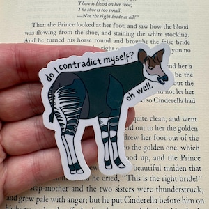 May include: A die-cut sticker featuring an okapi with a dark brown body and white striped legs. The text "do I contradict myself?" is arched above the animal, and the words "oh well." are printed in black near the okapi's head.