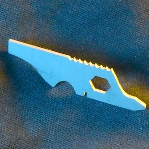 May include: A small, light blue multi-tool with a yellow edge. The tool has a serrated edge, a hexagonal hole, and a curved design. The tool is made of metal and is likely used for various tasks.