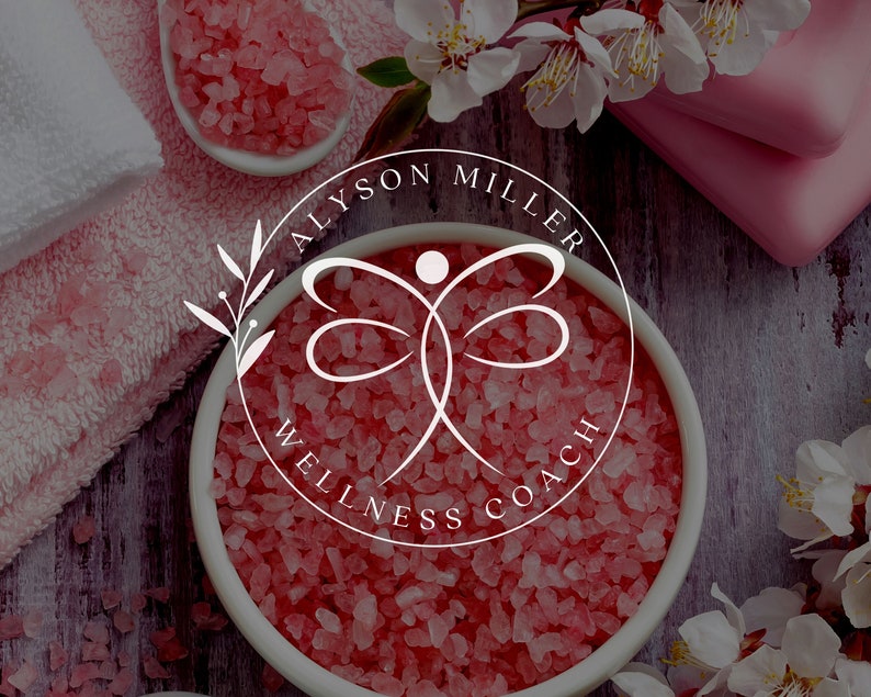 K&ouml;nnte beinhalten: Ein Bild zum Thema Spa mit einem wei&szlig;en Logo mit der Aufschrift "ALYSON MILLER WELLNESS COACH" in einem kreisf&ouml;rmigen Design. Das Logo befindet sich vor einem Hintergrund aus rosa Badesalzen, Handt&uuml;chern und Blumen, was eine ruhige und einladende Atmosph&auml;re schafft.