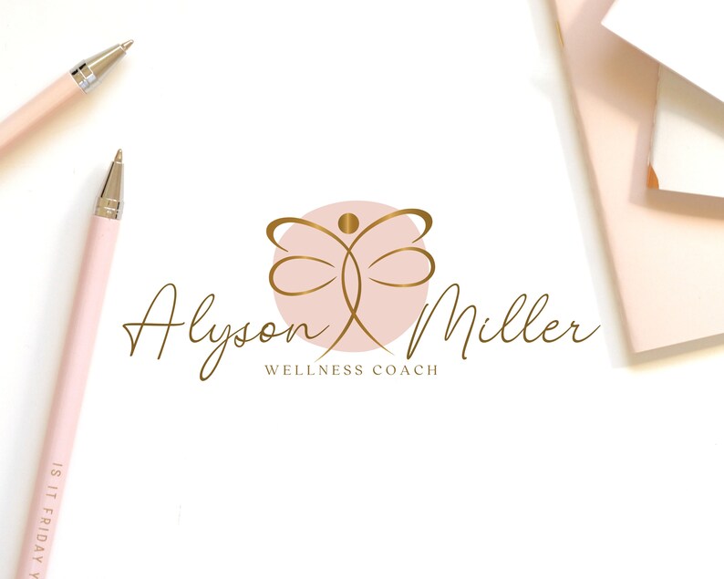 K&ouml;nnte beinhalten: Ein Logo mit einer goldenen abstrakten Figur in einem rosa Kreis, mit dem Namen "Alyson Miller" in goldener Schrift. Unter dem Namen steht der Text "Wellness Coach". Zwei rosa Stifte und ein Notizblock sind ebenfalls sichtbar.