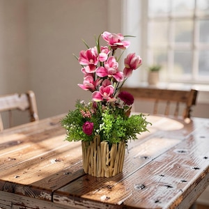 Op de afbeelding: Een bloemstuk met roze en witte bloemen, groen blad en donkerrode bloemen. De bloemen staan in een decoratieve houten vaas. Het arrangement staat op een rustieke houten tafel.