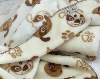 Könnte beinhalten: Weiße Fleece-Decke mit braunem Hundemuster und Pfotenabdrücken. Die Decke hat ein Etikett mit der Aufschrift "Macy & Eddie".