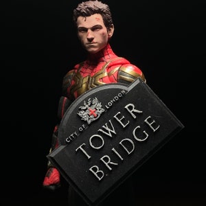 Può includere: Una action figure di Spider-Man rossa e dorata che tiene un cartello nero con la scritta "City of London Tower Bridge".