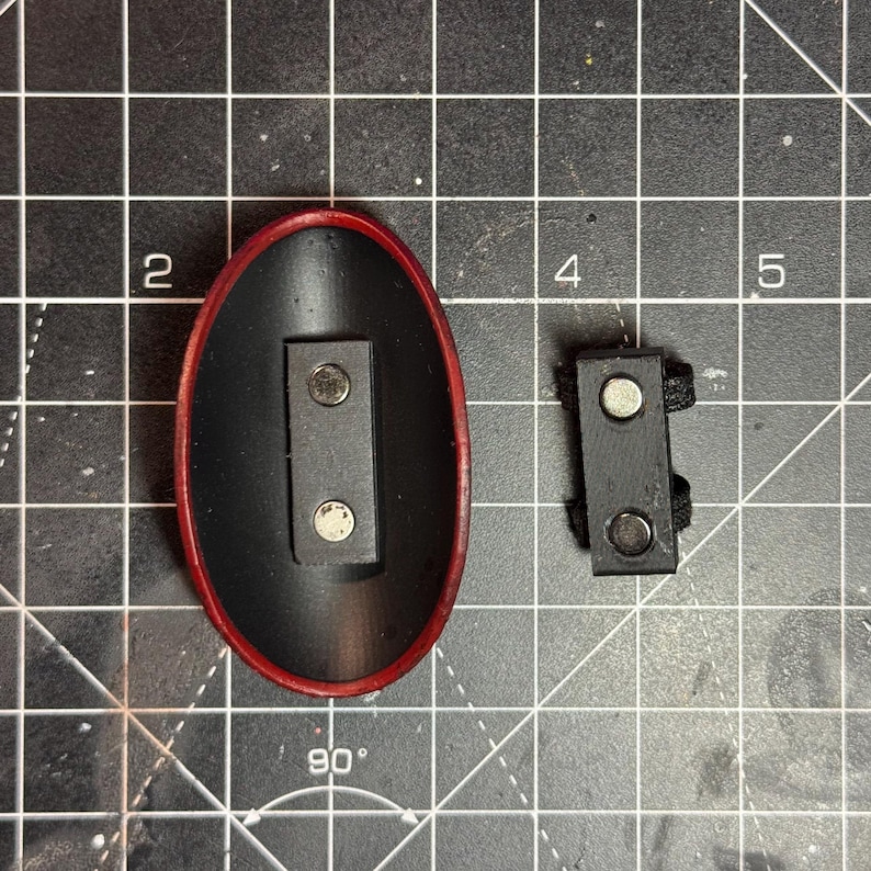 May include: Two black magnetic clasps. One is an oval shape with a red border, the other is rectangular with a black strap. Both have two silver magnets.