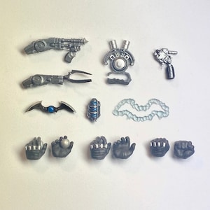 May include: A set of 11 action figure accessories, including a pair of black gloves, a pair of silver and black gauntlets, a silver and black grappling hook, a silver and black gun, a silver and black batarang, a silver and black device, a silver and black weapon, a silver and black device, and a clear plastic chain.