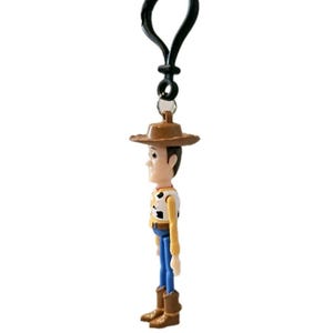 May include: A small, plastic Woody action figure keychain. The figure wears a brown cowboy hat, a yellow shirt with a black and white cow-print vest, blue pants, and brown boots. The keychain has a black clip.