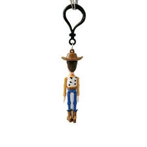 May include: A Woody character keychain. The miniature figure has a brown cowboy hat, a tan shirt with a black and white cow pattern, blue pants, and brown boots. The keychain has a black clasp.