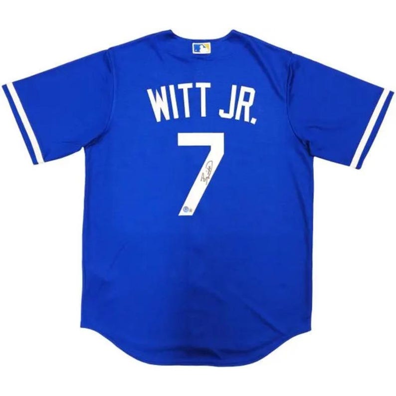 May include: Royal blue baseball jersey with white lettering and the name "WITT JR." and the number "7". The jersey has white stripes on the sleeves and a small logo on the upper chest.