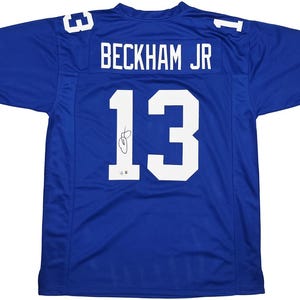 May include: A blue football jersey with the name "BECKHAM JR" and the number "13" in white. The number "13" is also on the shoulders. The jersey has a signature on the front.