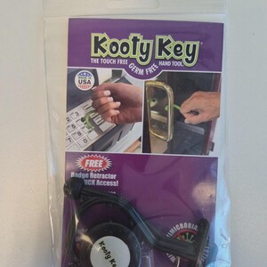 May include: A clear plastic package containing a black "Kooty Key" hand tool. The purple and white label reads "Kooty Key" and "The Touch Free Germ Free Hand Tool." The tool is designed for touch-free interaction with surfaces. Includes a free badge retractor.