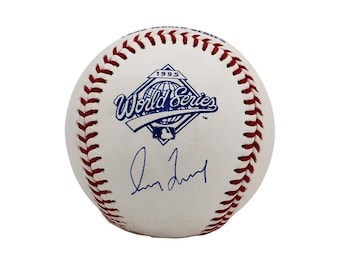May include: A white baseball with red stitching featuring a blue 1995 World Series logo printed on the surface. Below the logo, there is a blue ink signature written across the center of the ball. The baseball has a smooth leather texture.