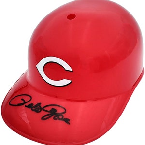May include: A bright red baseball helmet with a white "C" logo and a signature on the brim. The helmet has a glossy finish and a small vent hole on top. A collectible item for baseball fans.