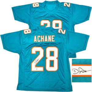 May include: A turquoise football jersey with the number 28 in white and orange. The name "ACHANE" is above the number on the back. The jersey has a V-neck and short sleeves. The number 8 is on each shoulder. A close-up shows a signature.