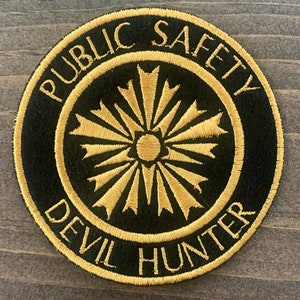 May include: A black and gold embroidered patch with the text "Public Safety Devil Hunter" in a circle.