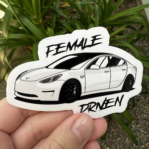 May include: White sticker with a black and white illustration of a car and the text "FEMALE DRIVEN".