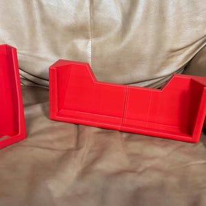 Könnte beinhalten: Zwei rote Kunststoff-Aufbewahrungsbehälter mit offenen Oberseiten. Die Behälter sind für die Aufbewahrung von kleinen Gegenständen wie Würfeln oder Spielsteinen konzipiert.