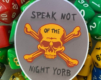 May include: A circular sticker with a gray background featuring a yellow skull and crossbones graphic. The text "SPEAK NOT OF THE NIGHT YORB" is printed in black lettering above and below the skull. The sticker is surrounded by various polyhedral dice.