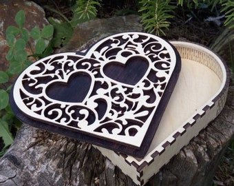 May include: A heart-shaped wooden box with a decorative, openwork lid. The lid features two heart cutouts and intricate scrollwork. The box is made of light-colored wood with a dark brown interior and sits on a tree stump.