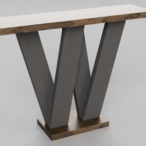 May include: A dark gray console table with a white top and a unique W-shaped base. The table has a brown wood trim around the top and base.