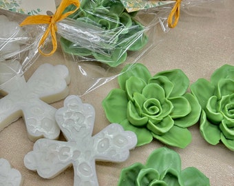 May include: White cross-shaped soaps with a textured design, packaged with green succulent-shaped soaps. The packaging includes a tag with the text "Faith Love Makes It Grow Oliver's Baptism 05/25/2021".