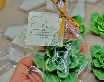 May include: A small green succulent plant in a clear plastic bag with a white cross and a tag that reads "Faith Love Makes It Grow Oliver's Baptism 03/25/2025".