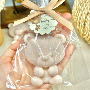May include: A small, white teddy bear soap in a clear plastic bag tied with a brown ribbon. The bag has a tag attached with the text "We Bearly Wait To Meet You" and a cartoon bear holding balloons.