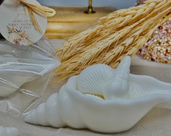 May include: White seashell shaped soap dish with a white seashell soap inside. The soap dish is on a white fabric surface.