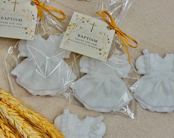 May include: White favor bags with small white dresses and a thank you card that reads "Christening Baptism Thank You for Celebrating with Us".