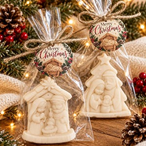 May include: Two clear plastic bags containing off-white molded soap figures of a nativity scene. Each bag is tied with twine and features a round tag with a nativity illustration and the text Merry Christmas in red and black script lettering.