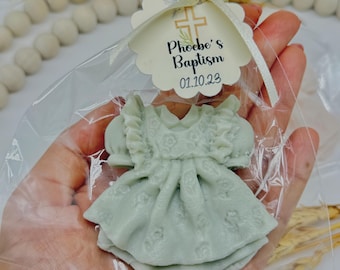 May include: A light green dress-shaped soap favor in a clear cellophane bag, tied with a cream ribbon and a tag that reads "Phoebe's Baptism 01.10.23". The soap has a detailed floral pattern.
