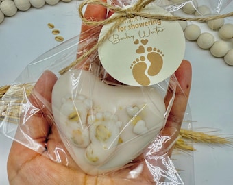 May include: A heart-shaped soap with baby footprints and small hearts, packaged in clear cellophane and tied with twine. A round tag reads "Thank you for showering Baby Water". The soap is white with tan accents.