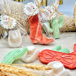 May include: A set of cowboy-themed party favors, including a cactus, a cowboy boot, and a cowboy hat. The favors are made of soap and are wrapped in clear cellophane bags. The bags are tied with twine and have a small tag that says "A Little Cowboy is on the Way".