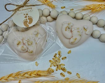 May include: Two heart-shaped soaps with baby footprints, one in a cellophane bag tied with twine. The soaps are light pink with white footprints. A tag reads "Thank You for showering Baby Water". Decorative wheat and wooden beads are also present.