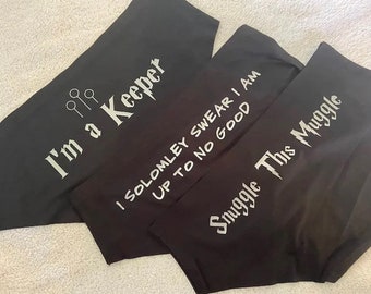 May include: Three black fabric items with white text. One reads "I'm a Keeper" with a graphic of quidditch hoops. Another says "I SOLOMLEY SWEAR I AM UP TO NO GOOD". The third says "Snuggle This Muggle".