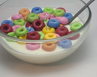 May include: A glass bowl filled with white milk and colorful cereal rings. The cereal is arranged in a random pattern and some of the rings are partially submerged in the milk. A silver spoon is resting on the edge of the bowl.