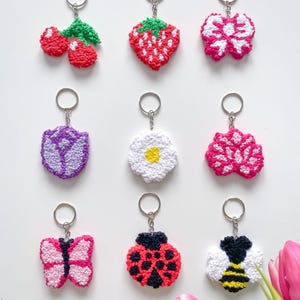 Peut inclure: Collection de porte-clés faits à la main, représentant des cerises, une fraise, un nœud, une fleur, un bouclier, un papillon, une coccinelle et une abeille. Chaque porte-clés est en fil texturé et possède un anneau argenté.