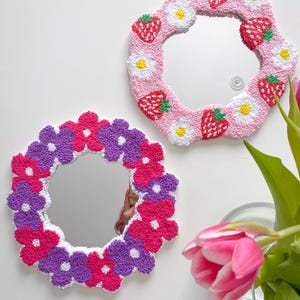 May include: Two decorative mirrors with floral and fruit designs. One mirror has a pink frame with strawberries and white daisies. The other mirror has a frame of pink, purple, and white flowers. Both mirrors are round.