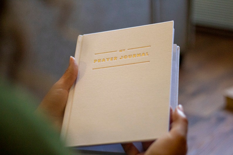 Puede incluir: Un diario de oraci&oacute;n blanco con letras doradas que dicen "My Prayer Journal".
