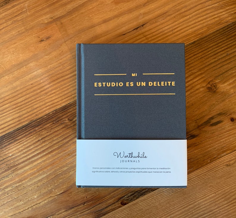 May include: A dark gray journal with gold lettering that reads "MI ESTUDIO ES UN DELEITE". The journal is wrapped in a white label with the text "Worthwhile JOURNALS" and a description in Spanish.
