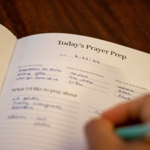 Puede incluir: Una libreta blanca con las palabras "Today's Prayer Prep" escritas en la parte superior. La fecha "4-23-22" est&aacute; escrita debajo del t&iacute;tulo. La libreta est&aacute; dividida en secciones para "Mis preocupaciones de hoy", "Por lo que estoy agradecido hoy", "Sobre lo que me gustar&iacute;a orar" y "Por qui&eacute;n puedo orar hoy".